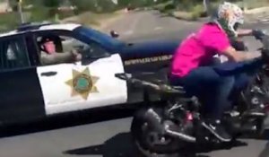 Un policier sort son arme pour un motard qui fait un wheeling sur la route
