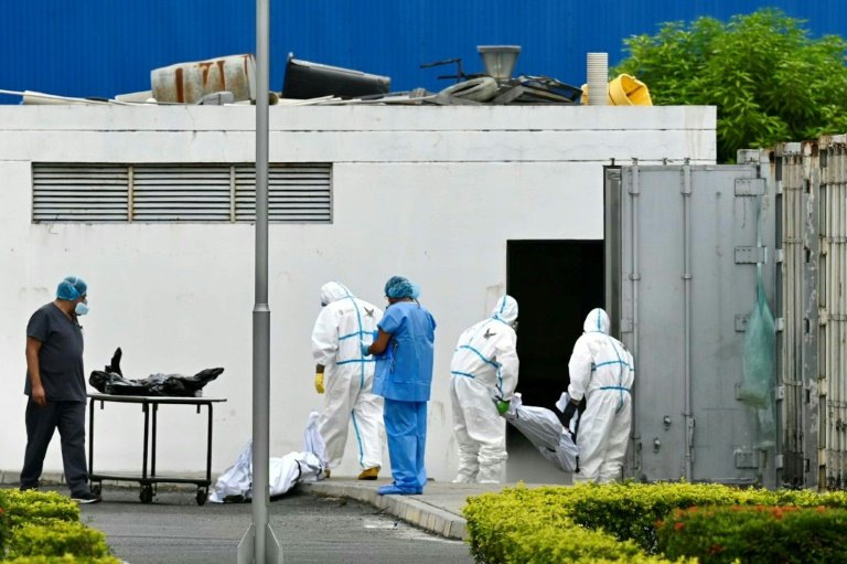 Des employés en combinaison sortent des sacs mortuaires d'un conteneur à la morgue de Guayaquil, le 14 juin 2024 en Equateur